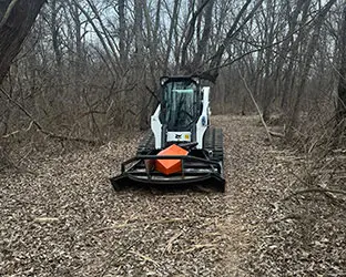 Bobcat loader with Brushcat rotary cutter attachment on cleared woodland trail